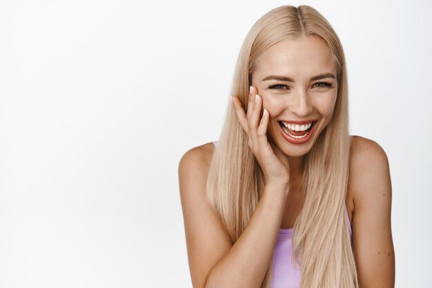 portrait-beautiful-blond-woman-smiling-laughing-touching-shiny-soft-facial-skin-standing-white-background-copy-space_176420-48725